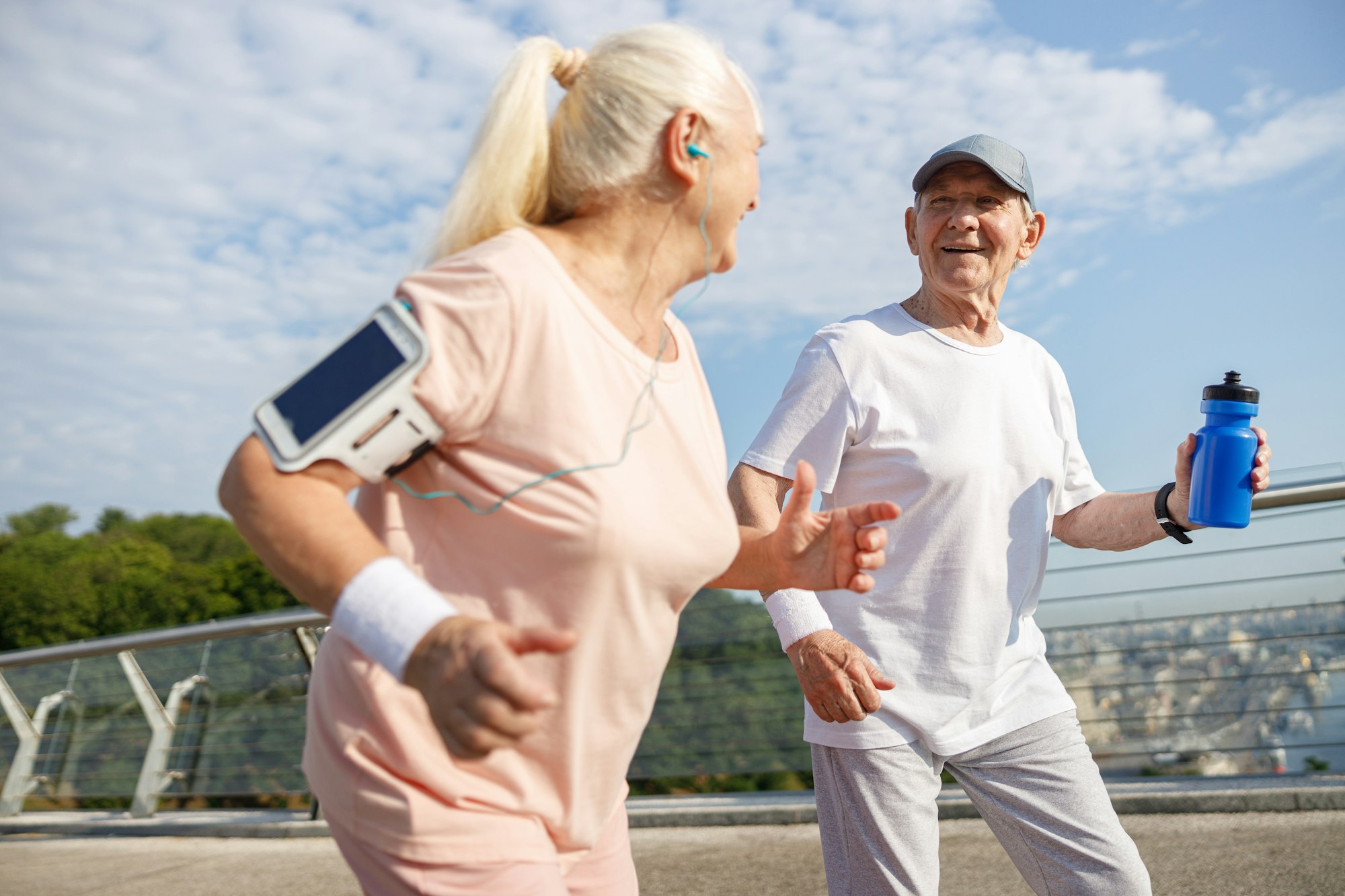 Mature man with bottle of water and wife run together along bridge